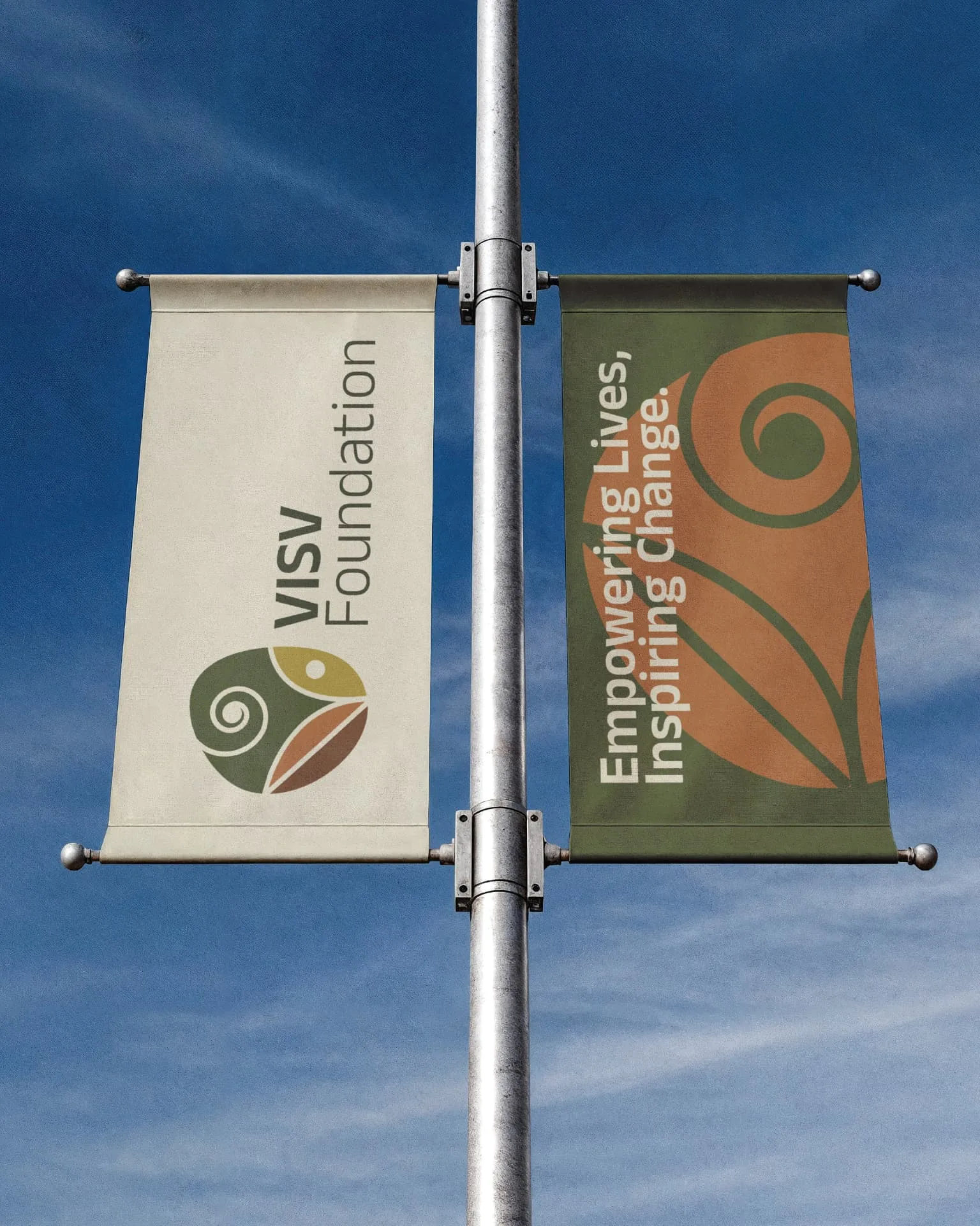Visv Foundation outdoor banners — paired lamppost flags against a blue sky carrying the VISV logo and the slogan “Empowering Lives, Inspiring Change”